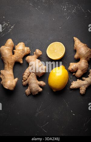 Ginger roots and whole and cut lemons creating a natural remedy concept. Healthy raw ingredients on dark textured surface Stock Photo