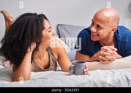 Couple Laughing Together in Bed: Cozy Morning Conversation and Relaxed Home Life Stock Photo