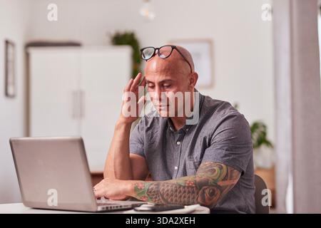Focused Professional Working On Laptop In Modern Home Office With Tattooed Arm And Glasses Stock Photo