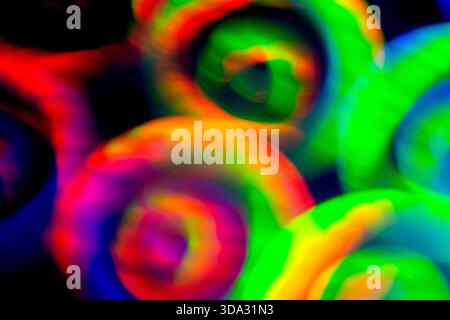 Abstract image of vivid swirling light circles in green, red, blue, yellow and pink tones on a dark background, with soft blur, glowing edges, layered Stock Photo