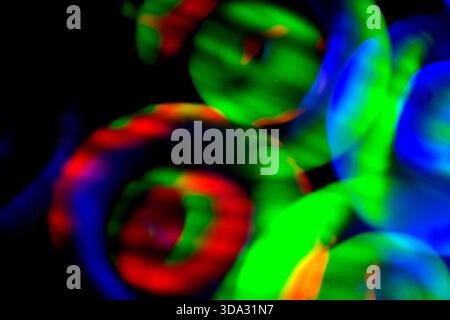 Abstract image of glowing circular light forms in green, red and blue tones on a dark background, with soft motion blur, overlapping shapes and vivid Stock Photo