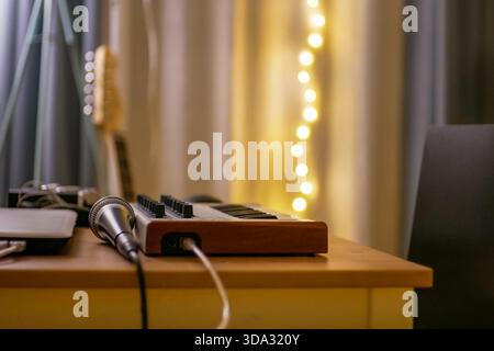 Cozy home music studio setup with MIDI keyboard, microphone, warm lights and creative workspace atmosphere for recording and production. Stock Photo