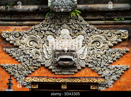 Intricate stone carving of a traditional Balinese Barong mask on a temple wall. Stock Photo