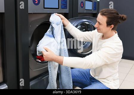 man puts blue jeans into a washing machine at a laundromat. High quality photo Stock Photo