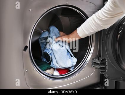 Close-up of a man's hand loading blue jeans and clothes into a modern washing machine. High quality photo Stock Photo