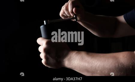 A man grinding beans using a hand coffee grinder. Milling handle process close-up on black background side view. Working male hands. Preparing drink Stock Photo