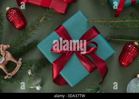 Overhead view of wrapped gift boxes with Christmas baubles, fir branches, pinecones and a Christmas tree ornament on a green background Stock Photo