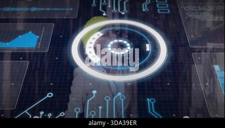 Standing engineer with yellow hard hat and blazer using circular HUD and graphs in control room Stock Photo