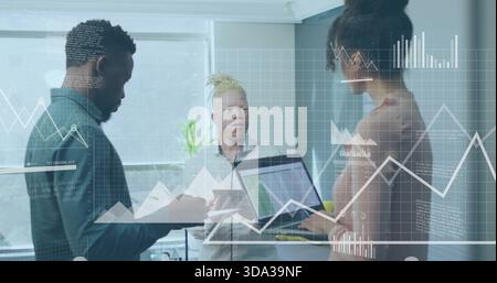 Reviewing data, team in business attire working in corner by window, with laptop, tablet and charts Stock Photo