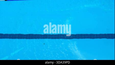 Displaying dark tiled lane marker stretching across clear blue pool interior, with scattered debris Stock Photo