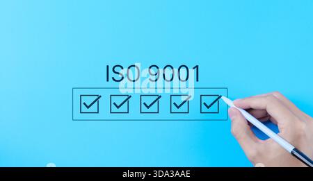 ISO 9001 Quality Assurance Checklist Concept. Hand marking checkboxes for ISO 9001 certification on blue background, symbolizing quality management an Stock Photo