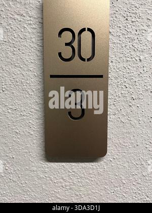 Golden metal apartment sign on white textured wall showing “30 / 3” number plate  Keywords: Stock Photo