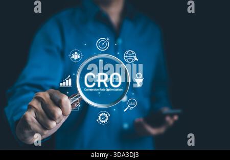CRO, Conversion Rate Optimization Concept. Businessman holding magnifying glass focusing on the text "CRO" with digital icons representing conversion Stock Photo