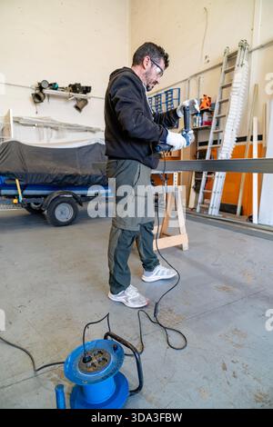 Skilled worker using an angle grinder on a metal profile in an industrial environment Stock Photo