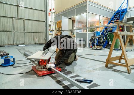 Worker operating a power tool, creating sparks while cutting a metal bar in a workshop Stock Photo