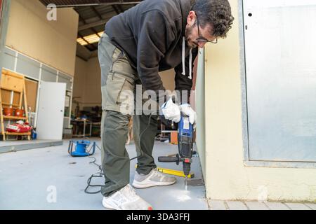 Man using electric drill making a hole in the floor of a workshop Stock Photo