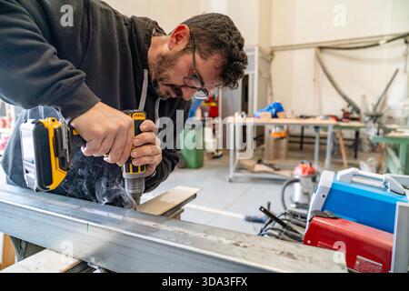 Man actively drilling a hole in a metal beam with a cordless drill in a workshop Stock Photo