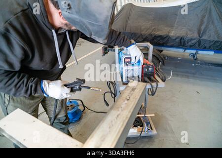 Welder working on a metal beam, wearing a safety mask and gloves Stock Photo