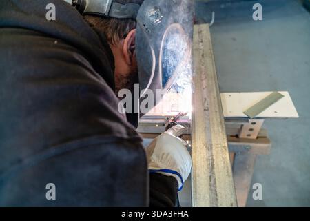 Welder wearing protective gear working on a metal structure in a workshop Stock Photo