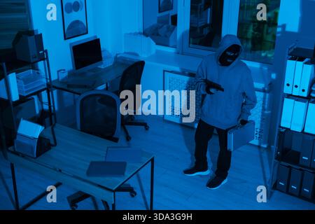 Thief with gun and briefcase in office at night Stock Photo