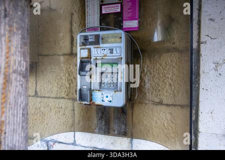 STOMORSKA, CROATIA, 10.24.2025:Aged, rust-speckled public payphone fixed to a weathered stone wall outdoors. The worn keypad and loose wires evoke nos Stock Photo