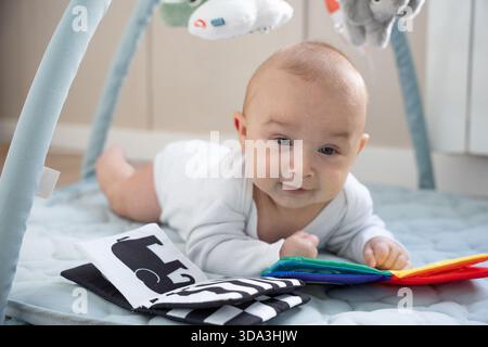 Cute infant looking up while playing with sensory toys during tummy time Stock Photo