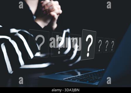 Question Marks and Problem Solving Concept. A person sits in front of laptop, surrounded by floating question mark icons, symbolizing inquiry, Stock Photo