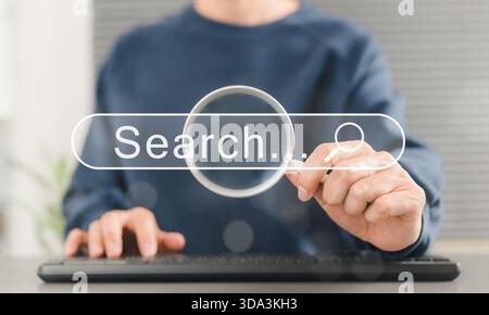 SEO search engine optimization concept. Person uses keyboard while holding magnifying glass with search bar labeled "Search", online search engine Stock Photo