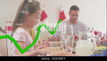 Praying girl at left in pink T-shirt sitting at home dining table, green graph overlay Stock Photo