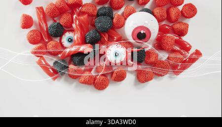 Showing top-down candy on white table, raspberry or blackberry, licorice, 3 eyeballs, dotted-wave Stock Photo