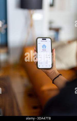 Woman using mobile app to control smart home devices, including lights, thermostat, security, and locks, enjoying modern living and convenience Stock Photo