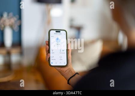 Woman using mobile app to control lights, thermostat, security, and locks in smart home environment Stock Photo