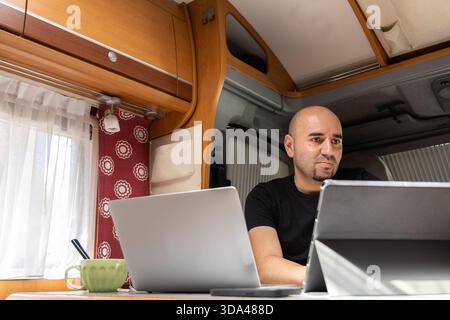Man working on a laptop inside a camper van while two pugs nap on the couch nearby. Stock Photo