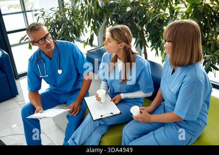 In a busy hospital, three dedicated healthcare professionals in scrubs discuss important medical documents, highlighting patient welfare and effective Stock Photo