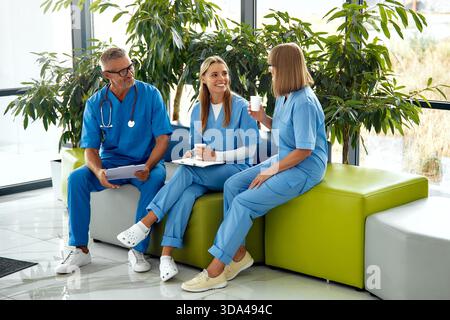 In a bright and inviting clinic, three dedicated healthcare professionals, each wearing scrubs, are engaged in a detailed discussion about patient car Stock Photo