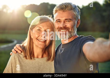 On a sunny day in a lively park, a cheerful elderly woman and a middleaged man take a selfie, cherishing their moments amidst the stunning nature, cap Stock Photo