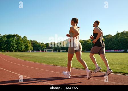 Fit young couple jogging together on stadium track in the morning. Healthy lifestyle, motivation and daily fitness routine concept in natural sunlight Stock Photo