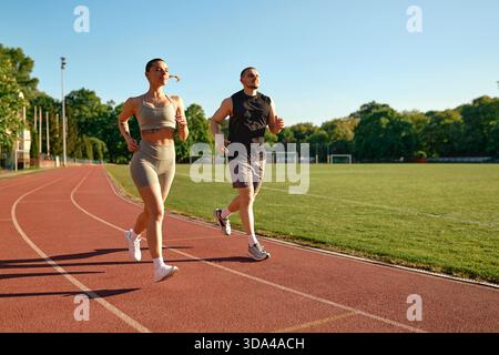 Fit young couple jogging together on stadium track in the morning. Healthy lifestyle, motivation and daily fitness routine concept in natural sunlight Stock Photo