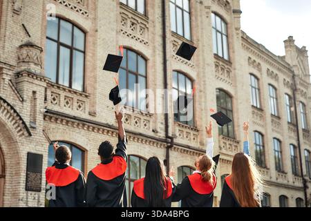 A group of graduates in academic attire rejoice in their achievement by throwing caps in the air outside a historic university building, celebrating s Stock Photo