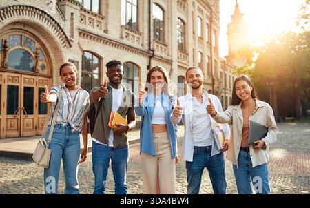 A vibrant and multicultural group of university students are outside, showing unity and positivity with thumbs up, representing a diverse community of Stock Photo