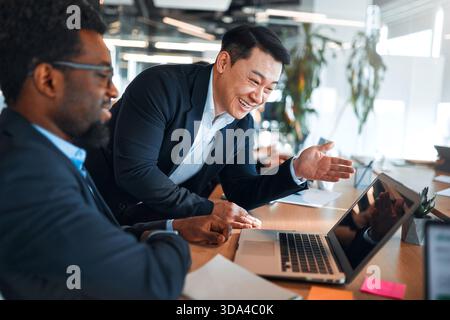 A team of young business workers in formal suits working with laptops while sitting in a modern office. Employees discussing a work plan or project on Stock Photo