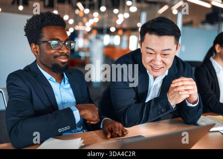 A team of young business workers in formal suits working with laptops while sitting in a modern office. Employees discussing a work plan or project on Stock Photo