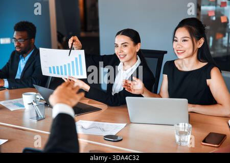 Team of young business workers working with charts, documents and laptops while sitting in a modern office. People working in a coworking space. Stock Photo