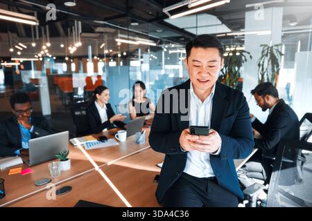 A team of young business workers in formal suits working with laptops while sitting in a modern office. Businessman in the foreground in a suit using Stock Photo