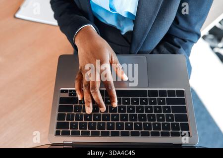 Cropped photo of african american woman holding laptop and typing on keyboard in modern office. People working in a coworking space. Stock Photo