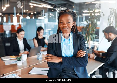 People working in a coworking space. African American woman smiling while standing in a modern office with a team of business workers in the backgroun Stock Photo