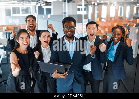 A team of successful businessmen of different nationalities in suits celebrating victory, success while standing in a modern office. Stock Photo
