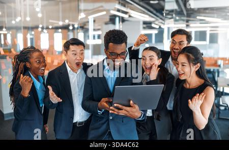 A team of successful businessmen of different nationalities in suits celebrating victory, success while standing in a modern office. Stock Photo