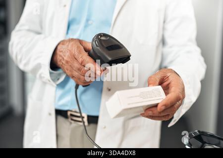 Close-up of an elderly pharmacist scanning a box of medication at the counter in a modern pharmacy. Concept: pharmacy workflow, technology in healthca Stock Photo
