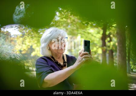 Happy senior woman using a smartphone for a selfie in a green park Stock Photo